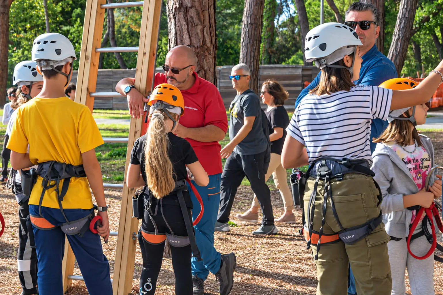 Gruppo di bambini e accompagnatori con casco e imbrago nel parco tra i pini